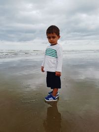 Boy standing on beach against sky