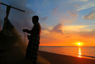 Side view of fisherman at beach during sunset