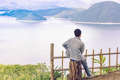 Rear view of man looking at lake against mountain