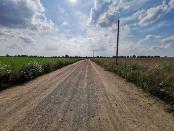 Dirt road amidst field against sky