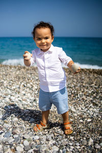 Happy kid in white shirt and blue shorts plays with pebble on the beach