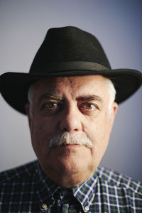 Portrait of serious senior man wearing black hat in front of grey background