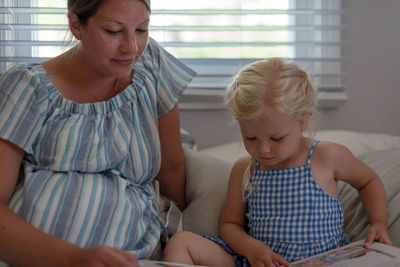 Mother and daughter reading picture book while sitting on sofa at home