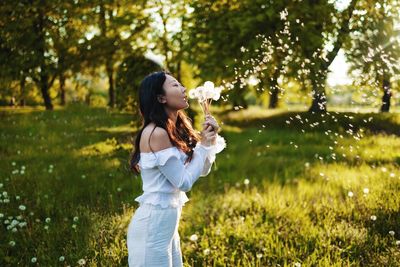 Girl blowing dandelion in field at sunset