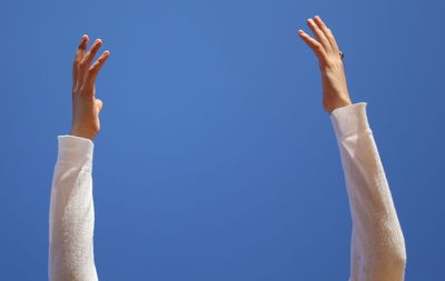 Low angle view of cropped woman with arms raised against clear blue sky