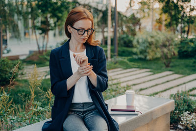 Young woman wearing sunglasses while sitting on bench in park