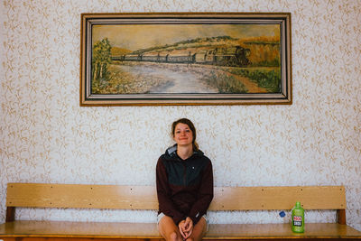 Portrait of a young woman sitting against wall