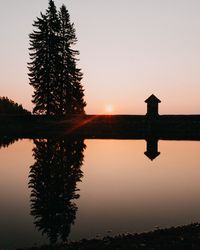 Silhouette tree by lake against sky during sunset