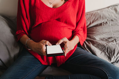 Midsection of woman using phone while sitting on bed at home