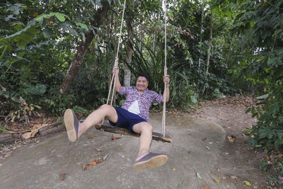 Portrait of man sitting on swing in forest