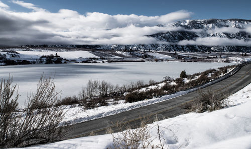 Road by frozen lake against cloudy sky during winter