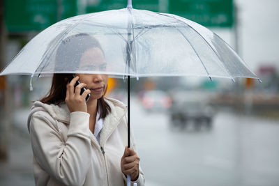 Woman holding mobile and umbrella on the street