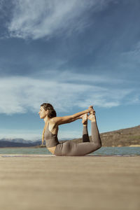 Young woman practicing dhanurasana on jetty