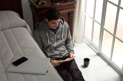 Young man using mobile phone while sitting on window