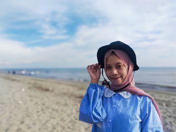 A girl is standing on the beach with the sea, waves and sky in the background