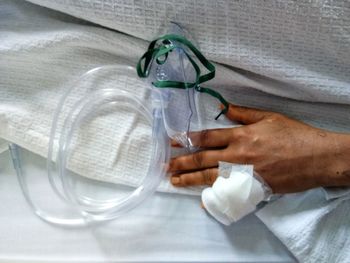 Cropped hand with oxygen mask on bed