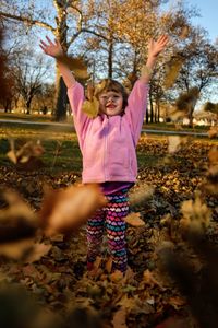 Full length portrait of girl throwing leaves on field