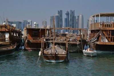 Boats moored at harbor against doha tower in city