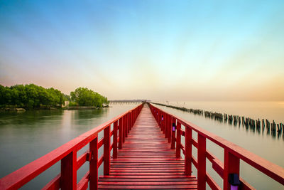 Wooden bridge over calm lake against sky