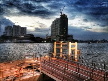 View of city at waterfront against cloudy sky