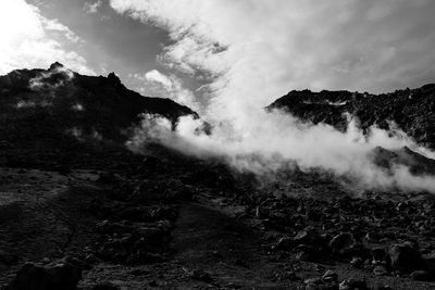 Steam emitting from volcanic landscape against cloudy sky