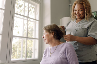 Low angle view of young female nurse brushing senior woman's hair at retirement home