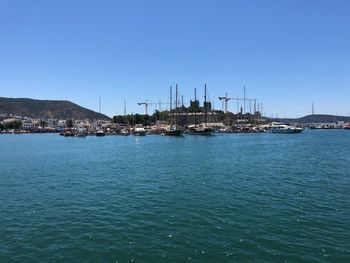 Sailboats in sea by buildings against clear blue sky