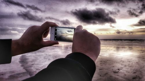 Cropped image of person on sea against cloudy sky