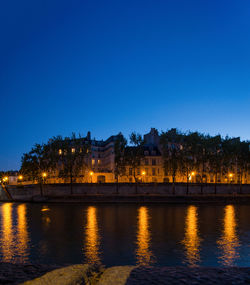 River by illuminated buildings against clear blue sky at night