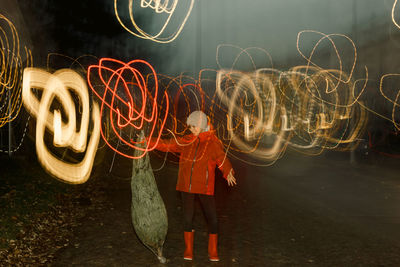 Girl with red jacket playin with a christmas tree with street lights effect
