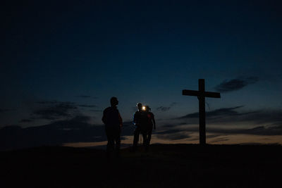 Silhouette friends standing on cross against sky