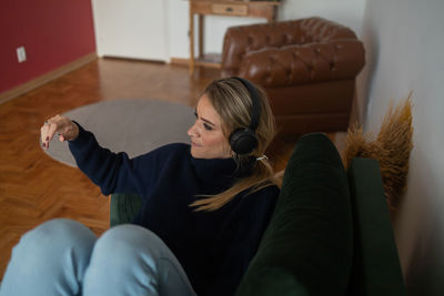 Woman listens to music with headphones lying down on her couch  mobile phone, urban living.