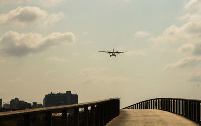 Low angle view of airplane flying over bridge against sky