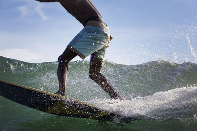 Low section of man surfing on sea