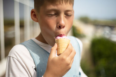 The boy is eating ice cream. pink strawberry ice cream in a waffle cup. enjoyment on a hot day. 