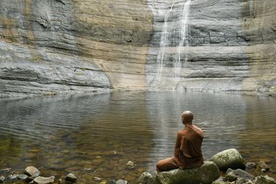 Rear view of man sitting on rock