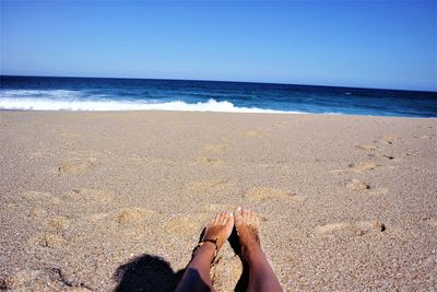 Low section of person relaxing at beach against sky