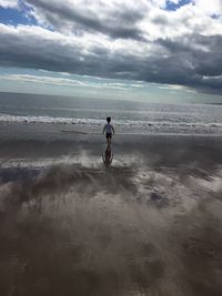 Rear view of boy walking on beach against sky