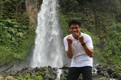 Portrait of smiling man standing against waterfall