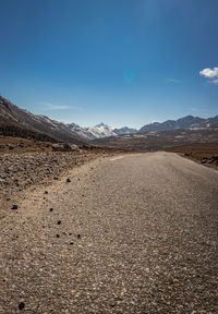 Road leading towards mountains against blue sky