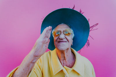 Senior woman wearing hat gesturing against pink background