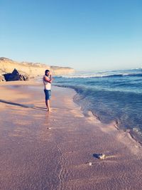 Side view full length of man standing on shore against clear sky at beach during sunny day