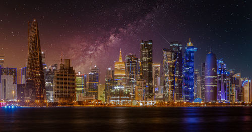 Illuminated modern buildings in city against sky at night