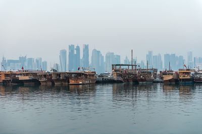 Boats in sea against buildings in city against clear sky