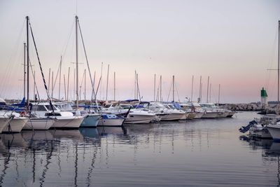 Sailboats moored in harbor at sunset