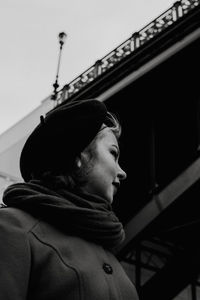 Low angle view of young woman looking away while standing against building in city