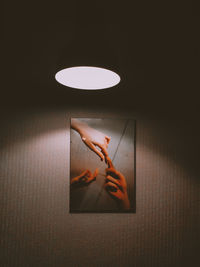 Close-up of hand on illuminated lamp against wall