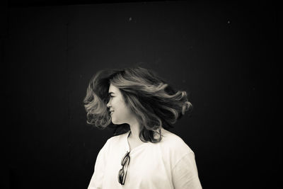 Happy young woman tossing hair against black background