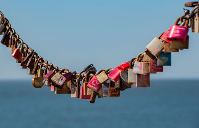 Close-up of love locks hanging on chain with sea in background
