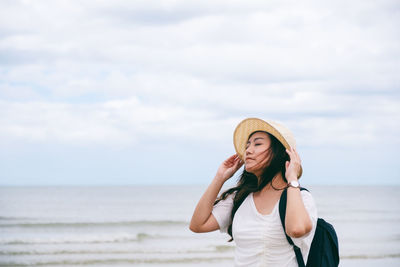 Young woman wearing hat standing at beach against sky